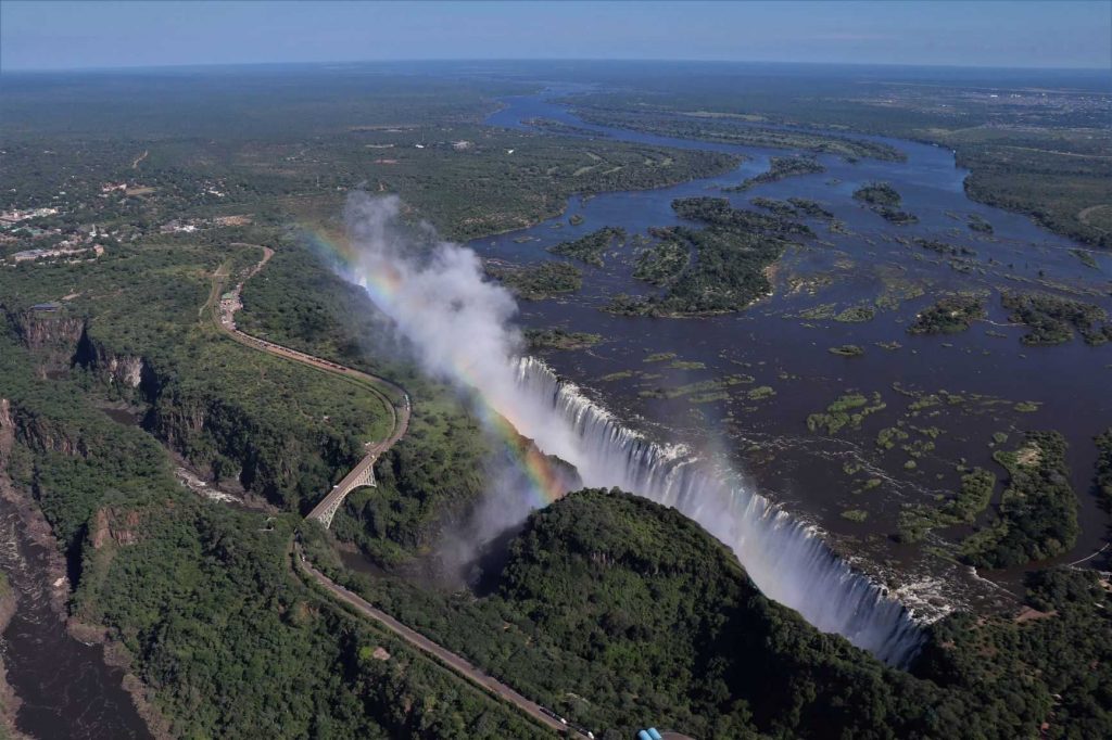 A breath-taking view of the entire length of the Vicotira Falls with a rainbow through the spray and the Zambezi River stretching away in the background.