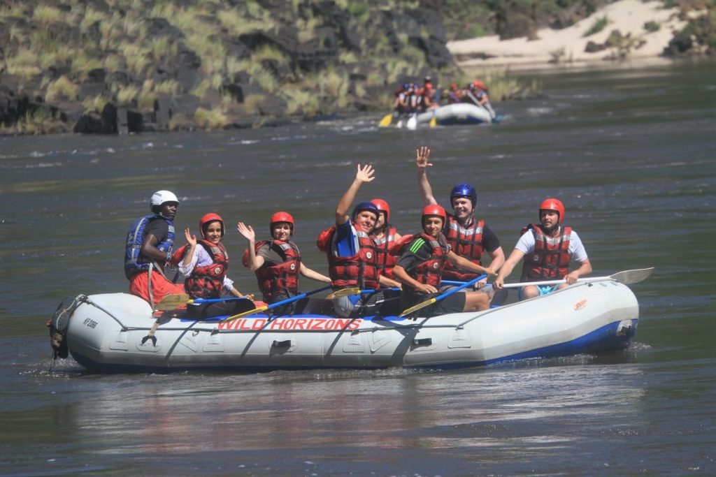 A lovely photo of everyone waving and smiling in calms waters, whitewater rafting Victoria Falls, Zimbabwe