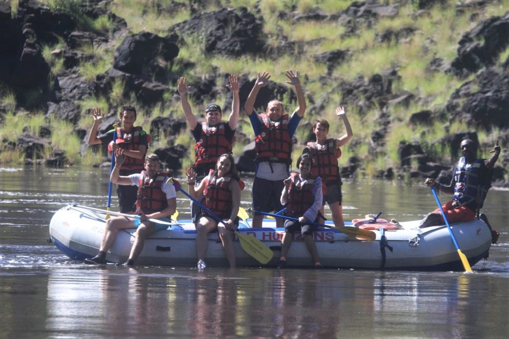 In the same calm waters some people are standing here and everyone is waving with a big smile on their face, whitewater rafting Victoria Falls