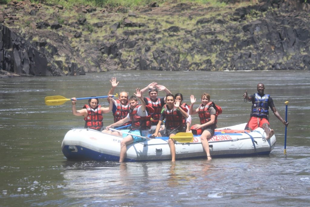 Kai in the front middle with everyone waving from the raft on a peaceful section of the Zambezi River, Zimbabwe