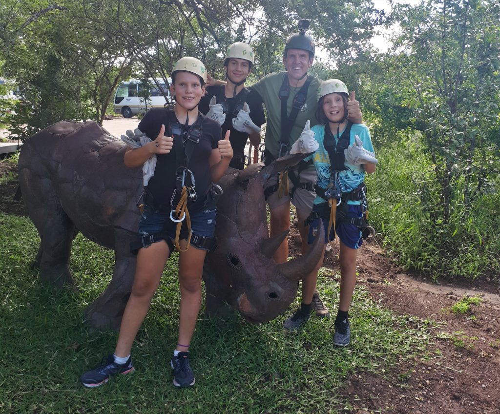 A lovely family photo of everyone kitted out with helmets and gear, showing thumbs up and standing around a rhino scultpure.