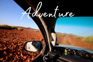 The word 'adventure' set over an image looking out of a self drive vehicle at the red rocky landscape of Damaraland in northern Namibia